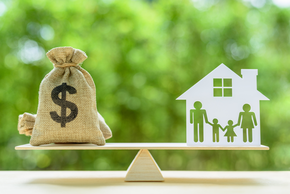 Family financial management, mortgage and payday loan or cash advance concept: Dollar bags, 4 members family under a house or shelter on a balance scale, depicts short term borrowing for a residence.