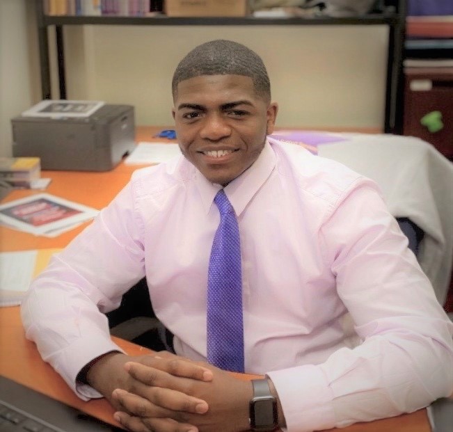 Jermaine Meadows sitting at desk wearing purple tie and pink shirt